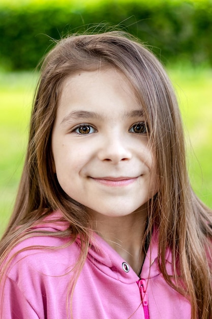 夏の公園の緑を背景にピンクのブラウスを着た美しい笑顔の魅力的なかわいい健康的な楽しい陽気な十代の女の子