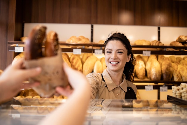 Beautiful smiling bakery worker selling pastry to the customer in bakery shop