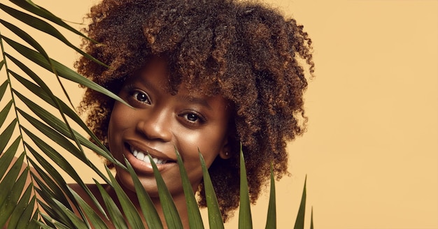 Foto bella donna sorridente di pelle nera con foglie tropicali esotiche verdi fresche ragazza di pelle nera tra foglia