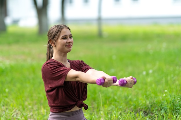 Beautiful smiling blonde girl holding dumbbells in her hands doing sports in the fresh air