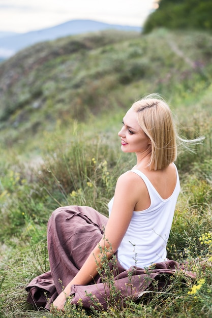 Beautiful smiling blonde young woman sitting on green grass