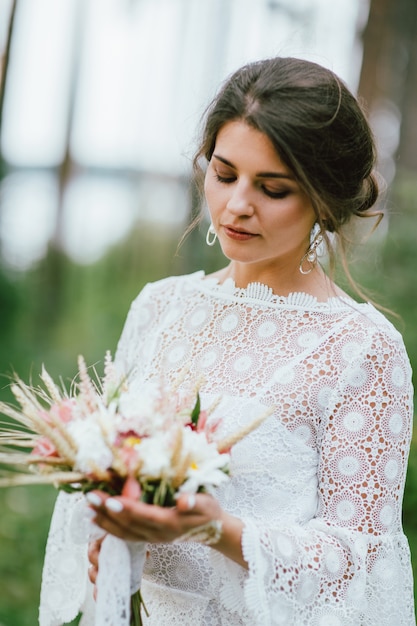 Beautiful smiling bride brunette young woman in white lace dress with wedding boho bouquet