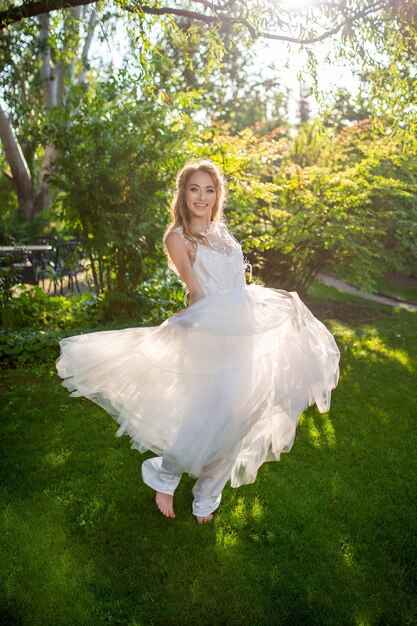 Фото Красивая улыбающаяся невеста в белом свадебном платье в саду крутится