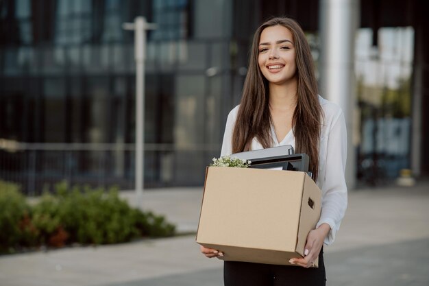 Beautiful smiling brunette girl in a shirt stands in front of the glass modern building