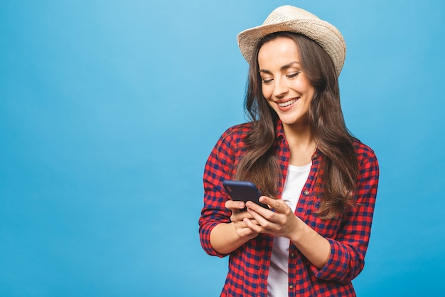 Красивая улыбающаяся брюнетка женщина в соломенной шляпе держит мобильный телефон, отправляя текстовое сообщение