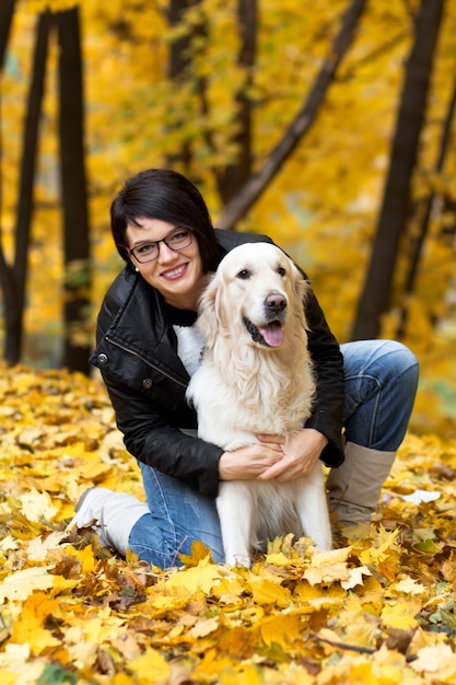 Beautiful smiling brunette woman with golden retriever in autumn park.