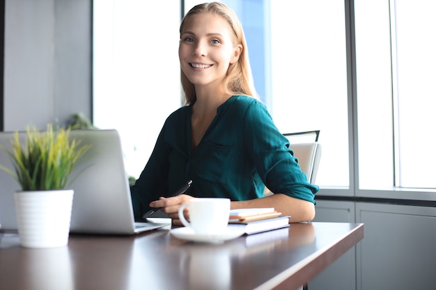 Beautiful smiling business woman is sitting in the office and looking at camera.