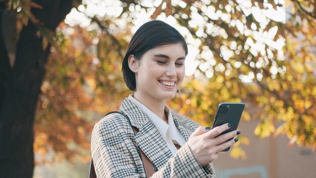 街の通りでスマートフォンでかなりの仕事に満足している美しい笑顔の実業家成功した女性