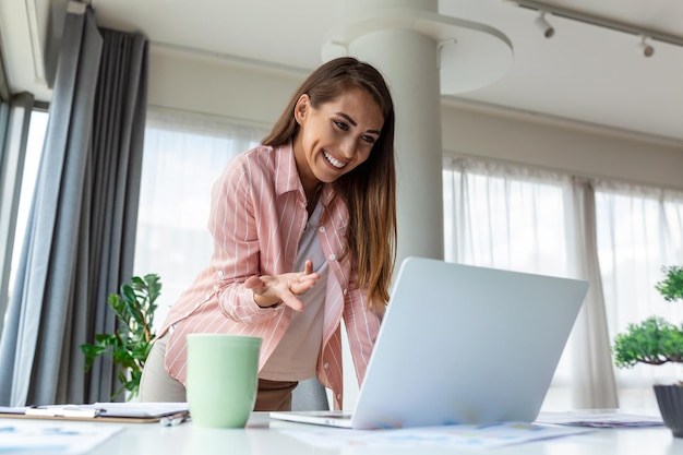 Beautiful smiling businesswoman reading something on a laptop while leaning on the table in the office