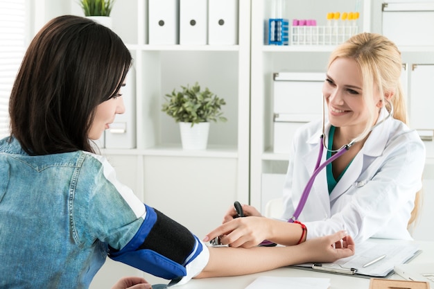 Beautiful smiling cheerful female medicine doctor measuring blood pressure to patient. Medical and healthcare concept