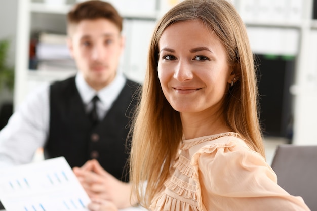 Beautiful smiling cheerful girl at workplace looking directly with colleagues group in background.