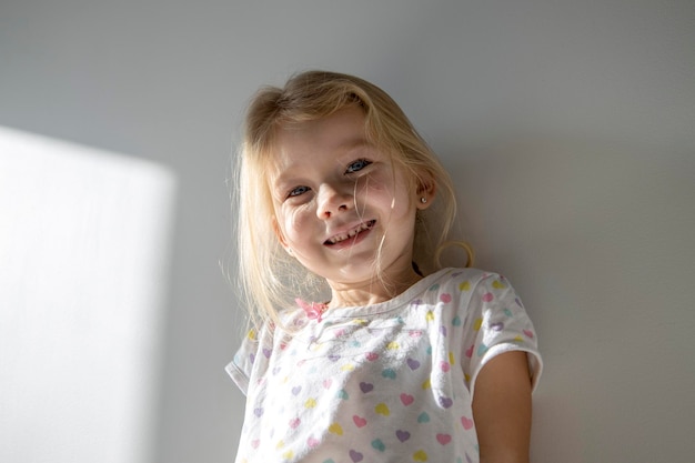 Beautiful smiling child girl blonde on the background of a white wall