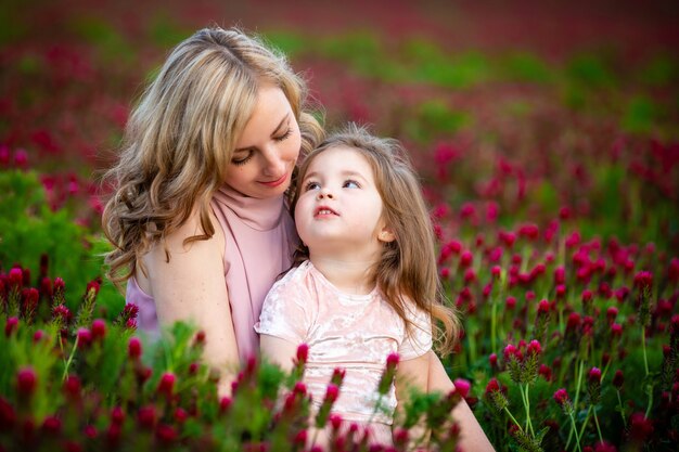 Beautiful smiling child girl with young mother in family look in field of clover flowers in sunset time