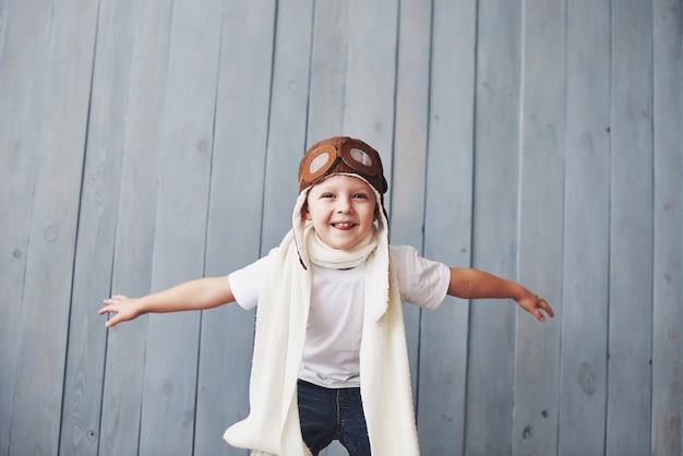 Beautiful smiling child in helmet on a blue background playing with a plane. Vintage pilot 