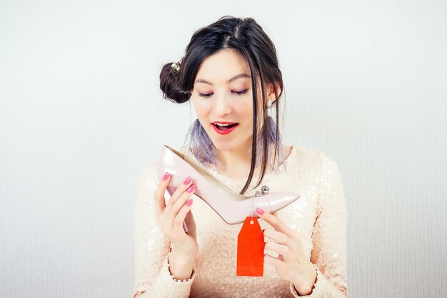 Beautiful smiling crazy brunette mad woman shopaholic holding a stylish pink shoes with a red label tag tab tally in her hand concept of seasonal sales and shopaholicism