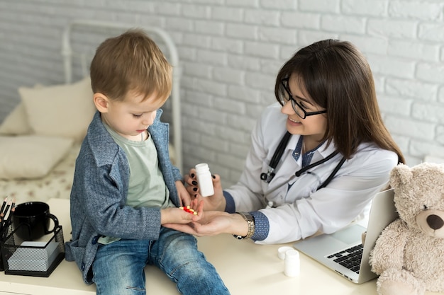 Il bello medico femminile sorridente tiene nella bottiglia della pillola delle armi e la offre al primo piano del visitatore del bambino.