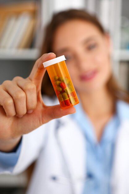 Beautiful smiling female doctor hold in arms pill bottle and offer it to visitor closeup.