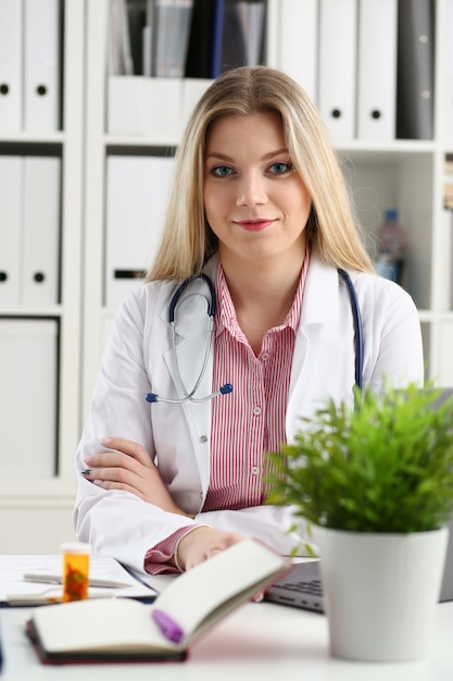 Beautiful smiling female doctor sit at workplace.