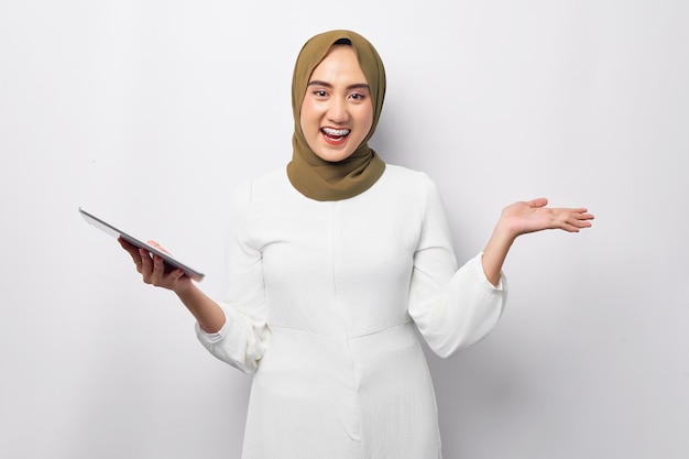 Beautiful smiling friendly young Arabian Asian Muslim woman wearing hijab green holding digital tablet and showing empt space with hand isolated on white background People religious lifestyle concept