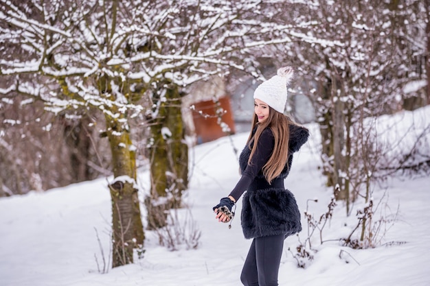 A beautiful smiling girl in black clothes and white hat in winter