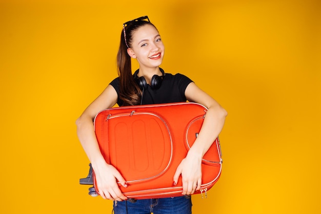 Beautiful smiling girl in a black t-shirt is going on vacation at sea, with a big red suitcase