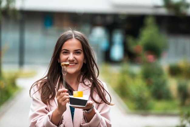 Una bella ragazza sorridente mangia poffertjes freschi mentre visita la città messa a fuoco selettiva