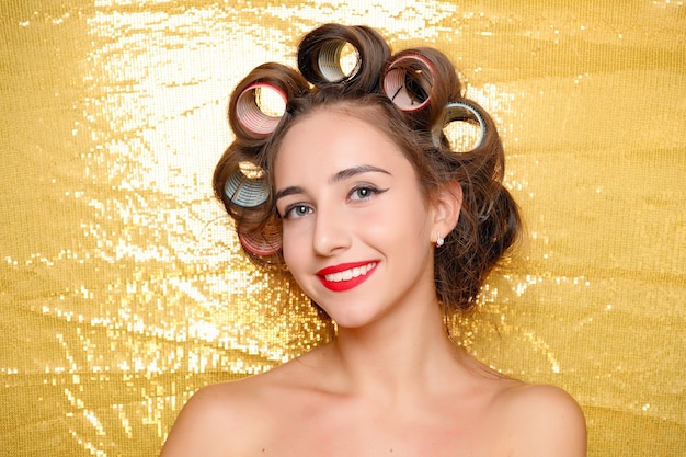 Beautiful Smiling girl in hair curlers isolated on gold. Portrait of young beautiful sexy smiling woman