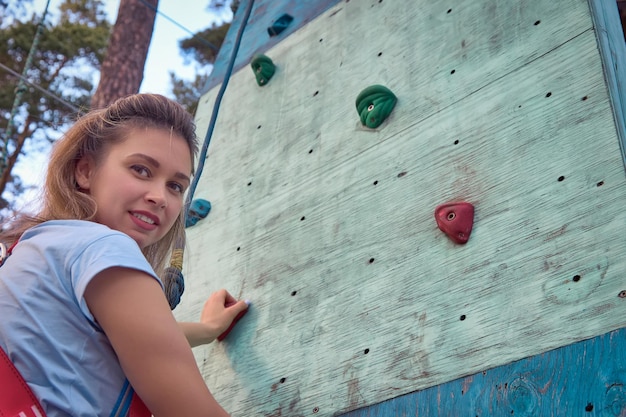 Beautiful smiling girl is preparing to climb up climbing wall located in forest