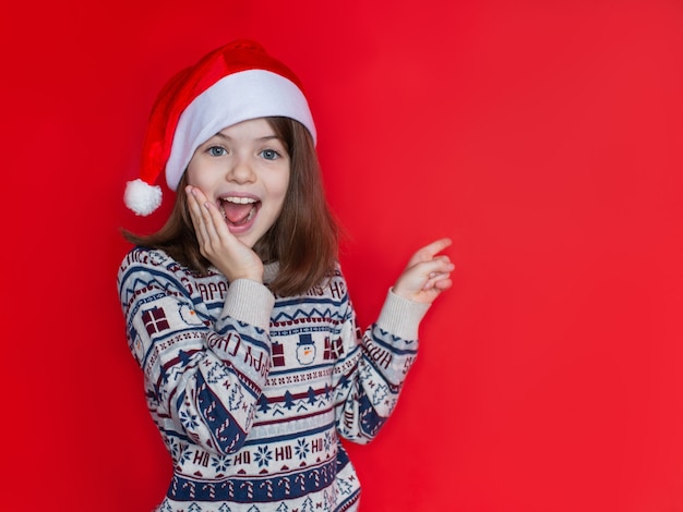 Beautiful smiling girl in a New Years sweater and Santa hat advertising New Year and Christmas concept