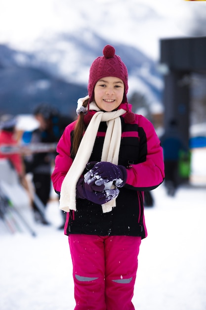 Beautiful smiling girl in pink ski suit posing against high mountain covered by snow