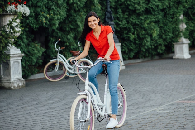 赤いTシャツを着た美しい微笑の女の子が白い自転車に乗る