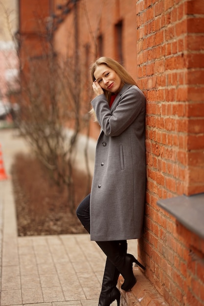 A beautiful smiling girl stands next to the red bricked wall