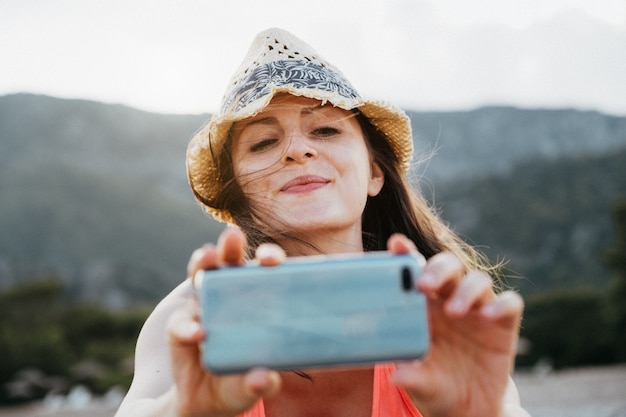 Beautiful smiling girl taking a picture with her smartphone at sunset over mountain