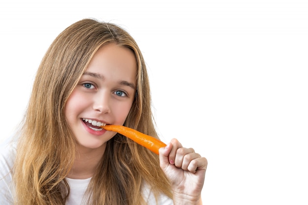 Beautiful smiling girl with long hair in a white shirt bites carrots isolated