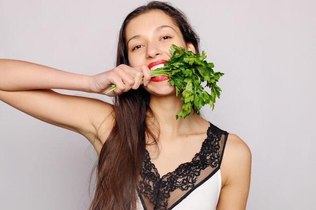 Beautiful smiling girl with parsley. Photo of fashion female on gray