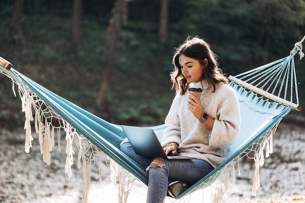 Beautiful smiling girl working on laptop in the park on a hammock