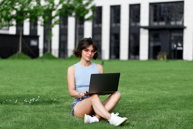 公園でMacbookProと一緒に働いている美しい笑顔の女の子