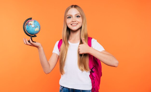 Beautiful smiling and happy school girl with backpack is posing on yellow background