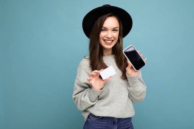 Bella giovane donna castana felice sorridente che porta cappello nero e maglione grigio