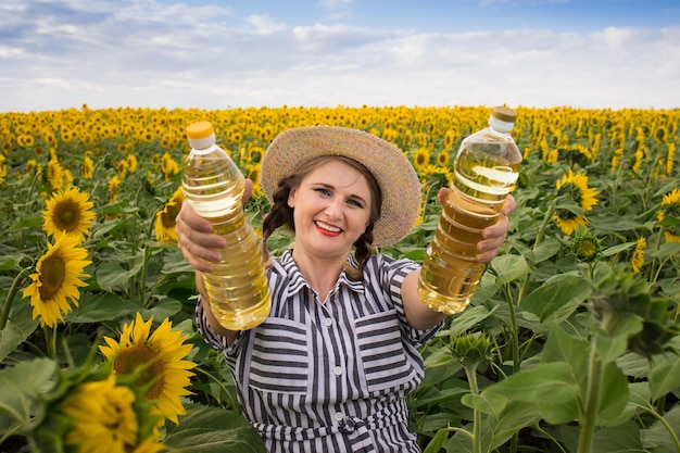 Beautiful smiling joyful middleaged farmer woman holding bottles of golden sunflower oil in her hands in a harvest field of sunflowers on a sunny day