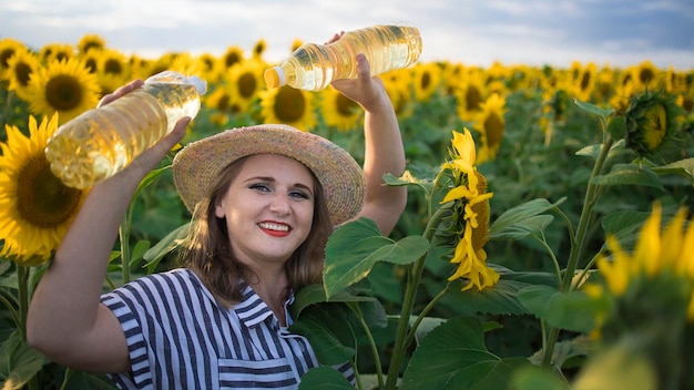 Beautiful smiling joyful middleaged farmer woman holding bottles of golden sunflower oil in her hands in a harvest field of sunflowers on a sunny day