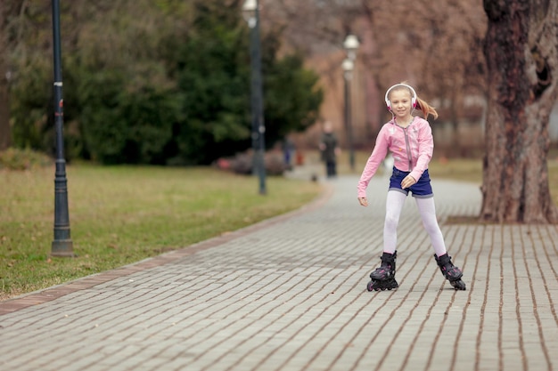 Beautiful smiling little girl inline skating through the park. Looking at camera.