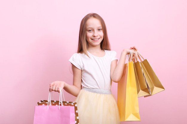 Beautiful smiling little girl with bags for shopping on a colored background