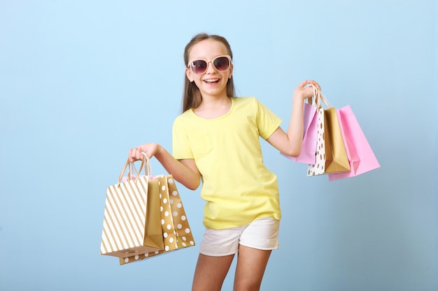 Beautiful smiling little girl with bags for shopping on a colored background