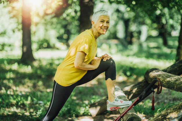 Beautiful smiling mature woman stretching legs after nordic walking exercise