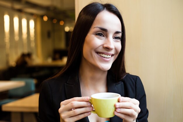 カフェに座って、ランチタイムにコーヒーやお茶を飲む美しい笑顔のモダンなビジネスウーマン