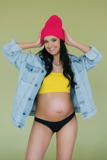 Photo beautiful smiling pregnant woman in a pink hat and bright stylish clothes on a green background              person