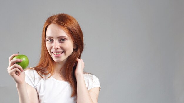 신선한 녹색 사과 들고 흰 셔츠에 아름 다운 웃는 빨간 머리 소녀.