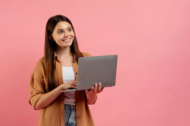 Beautiful smiling teen girl holding laptop and looking aside at copy space