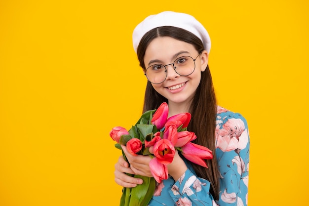 Beautiful smiling trendy teen girl with bouquet of tulips on yellow studio background Girl enjoying flowers